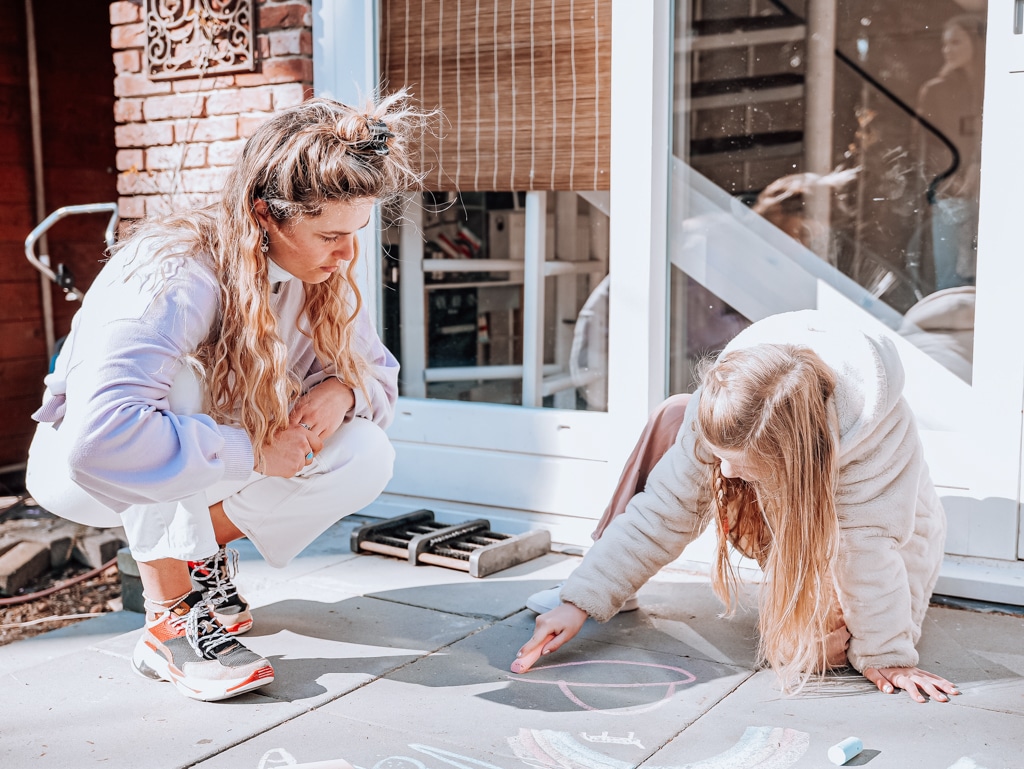 An au pair draws chalk art outside with her host children. Au pair requirements for the Netherlands.