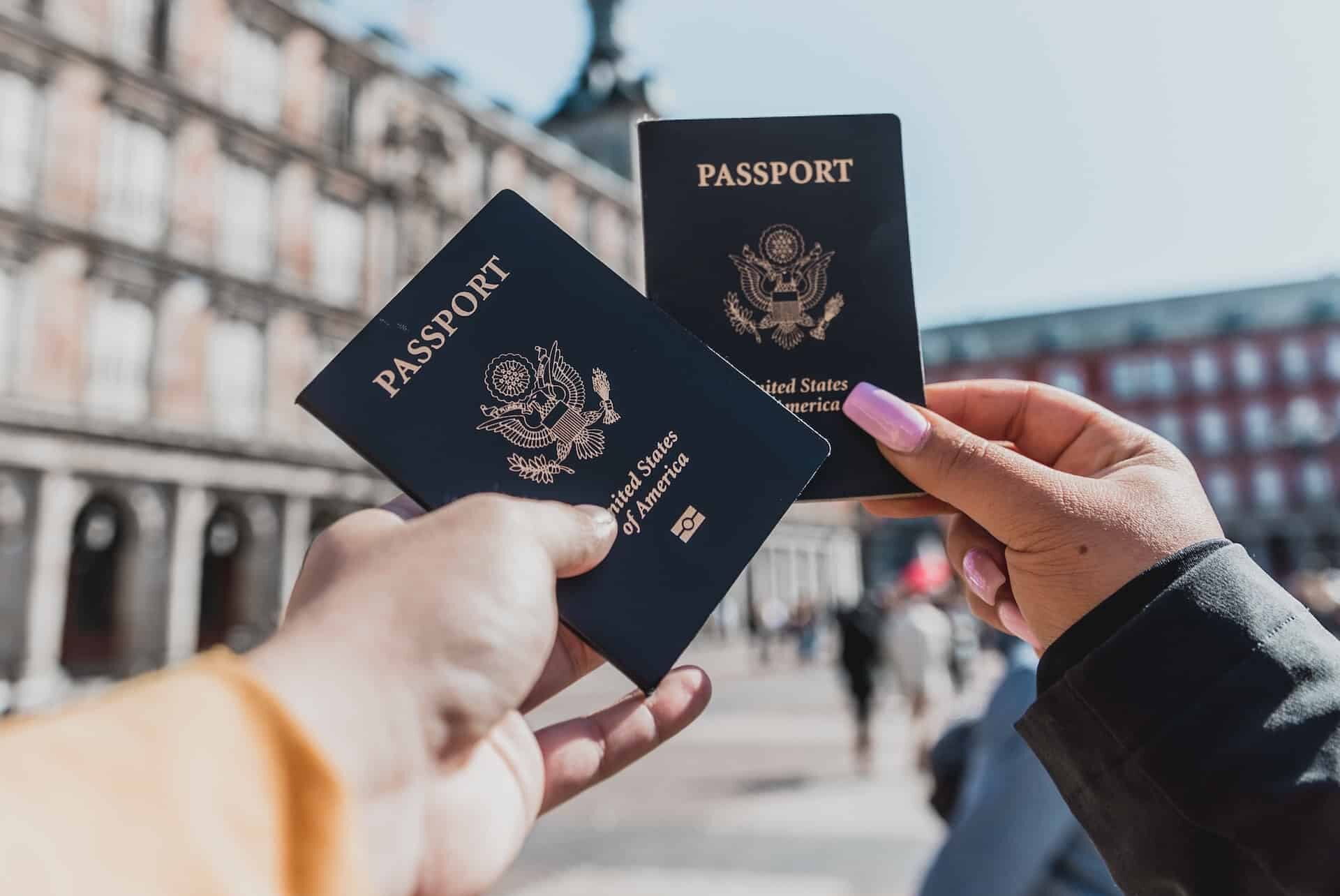 Two people hold their passports out in front of a pretty view while traveling.