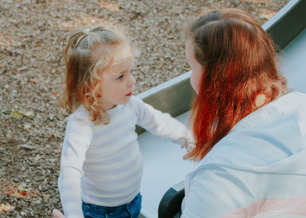 An au pair holds hands with one of her host children while playing at the playground. Au pair requirements for Belgium