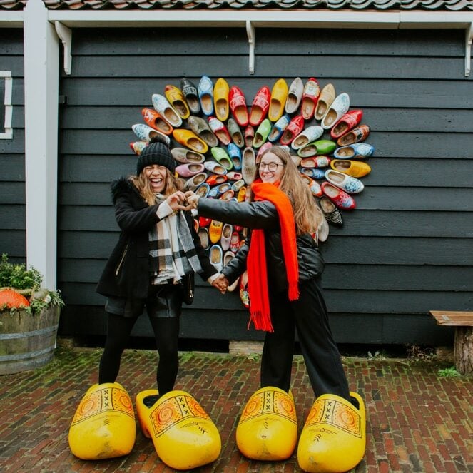 two au pairs in the netherlands pose together in wooden shoes during a visit to the old dutch village of zaanse schans.