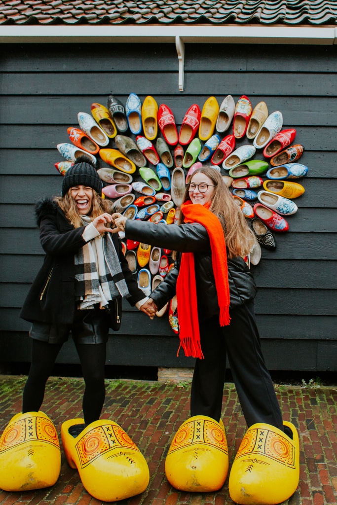 Two au pairs in the Netherlands pose together in wooden shoes during a visit to the old Dutch village of Zaanse Schans. Conditions to au pair in The Netherlands