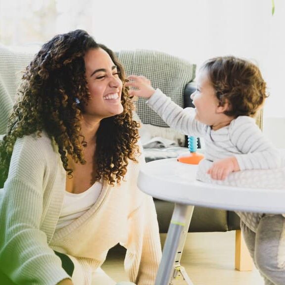 An au pair plays with her host child, an infant, in the living room.