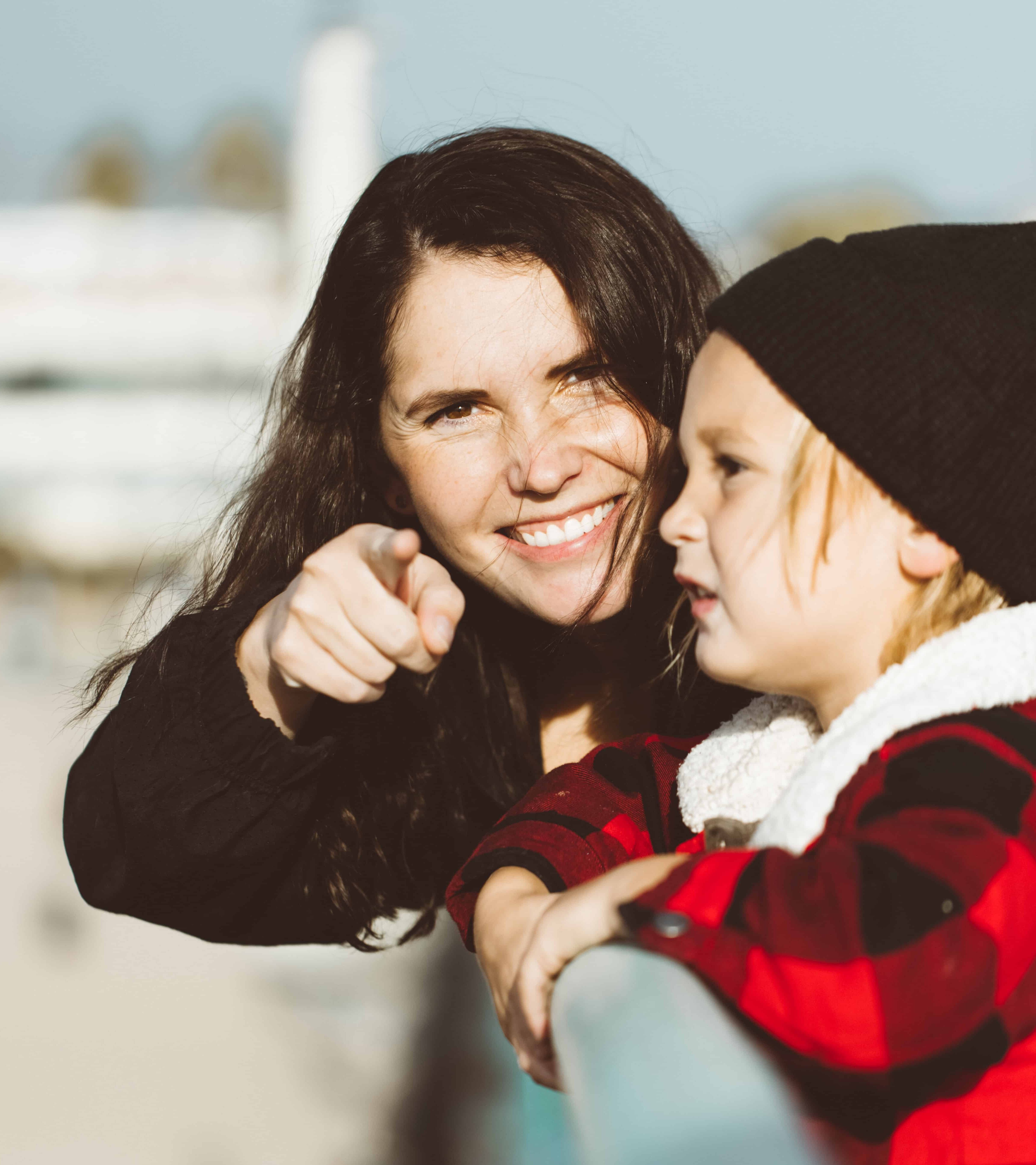 Want to know more information about au pairing or our au pair program? In this photo you see a girl pointing at the camera with a little kid standing next to her.