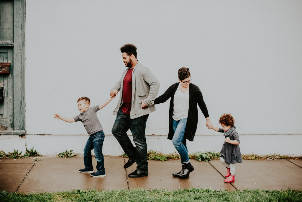 A mother and a father hold hands with their two children while walking together outside.