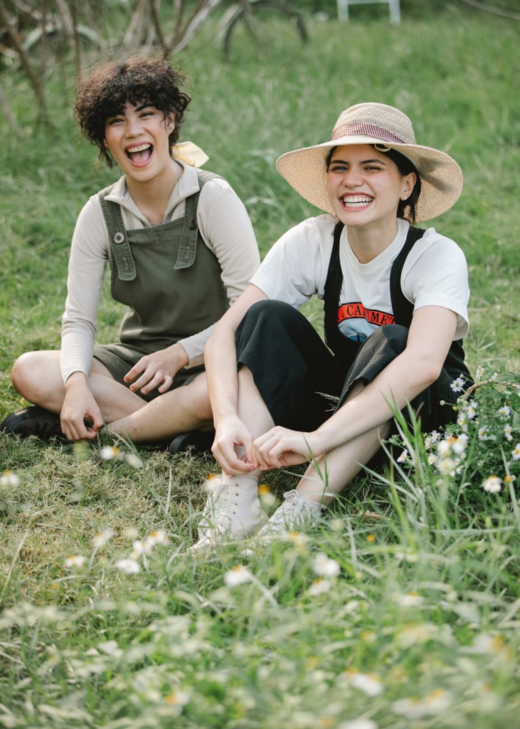 Two au pairs sit together in a beautiful green grass field with some wildflowers in Sweden. Conditions to au pair in Sweden