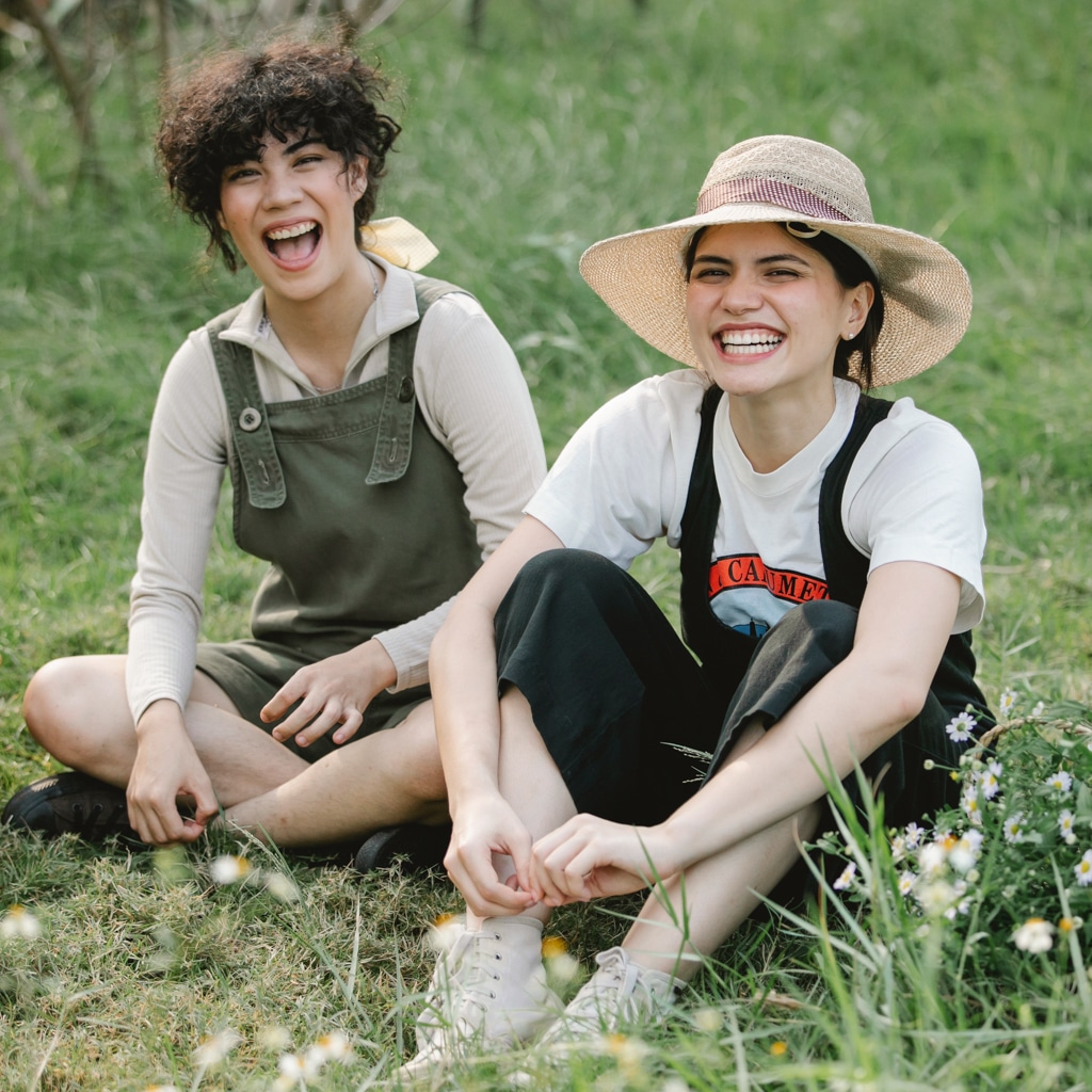 Two au pairs sit together in a beautiful green grass field with some wildflowers in Sweden.
