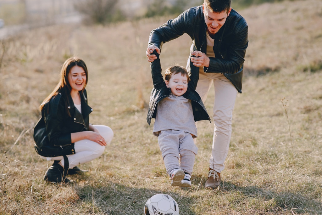 Parents play football outside with their toddler.