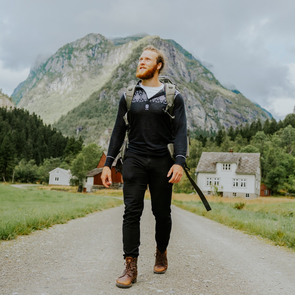 An au pair stands with his backpack and hiking shoes while visiting a small village in Norway.