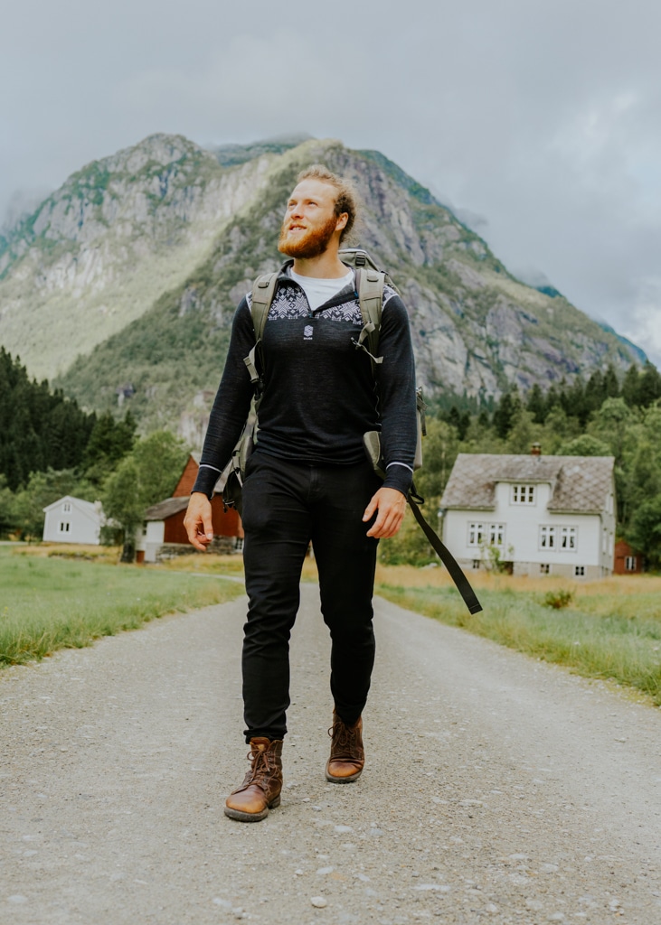 An au pair stands with his backpack and hiking shoes while visiting a small village in Norway. Conditions to au pair in Norway