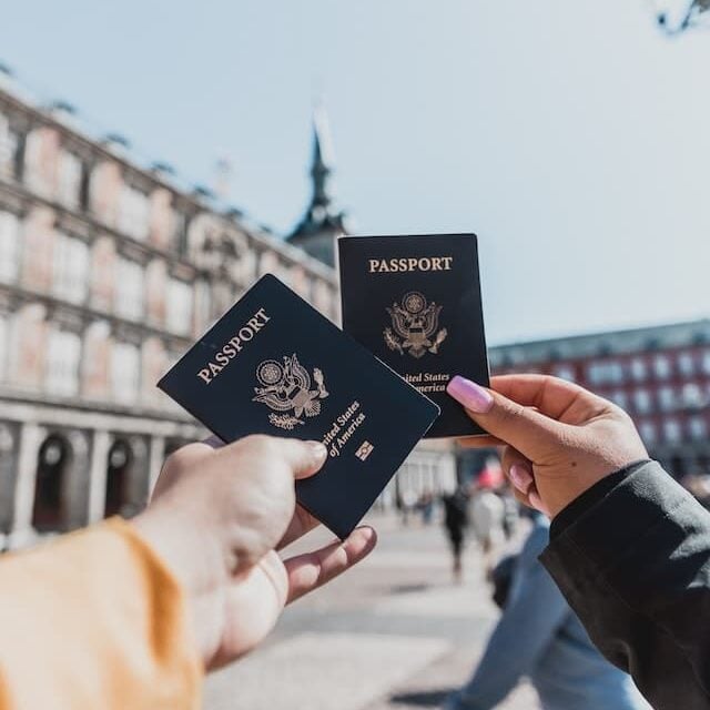 Two people hold their passports out in front of a pretty view while traveling.