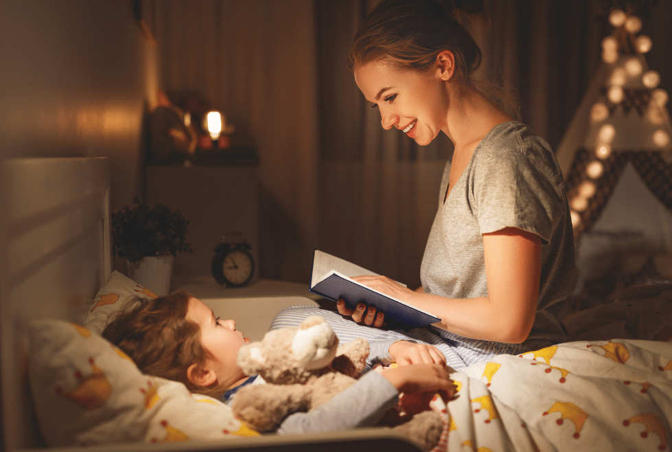 moeder die bij haar kindje op bed zit een verhaal voorleest uit een boek als bedritueel