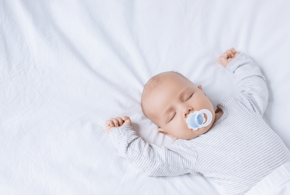 baby slaapt in een bedje met zijn handjes om hoog en een speen in de juiste slaapomgeving voor een kind