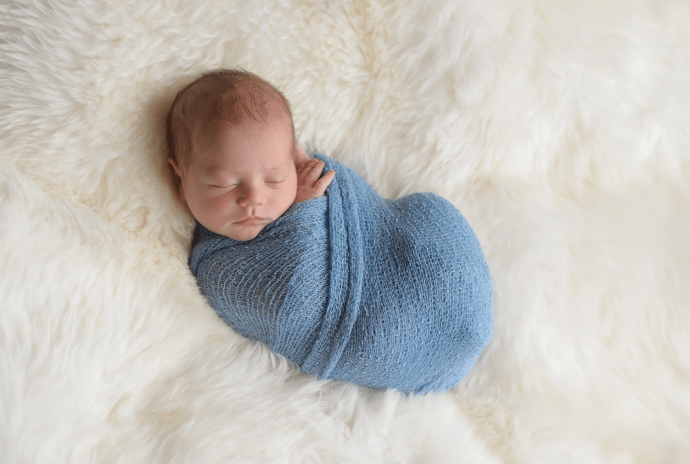 baby die in een blauw doek op een wit pluizig kleed ligt 