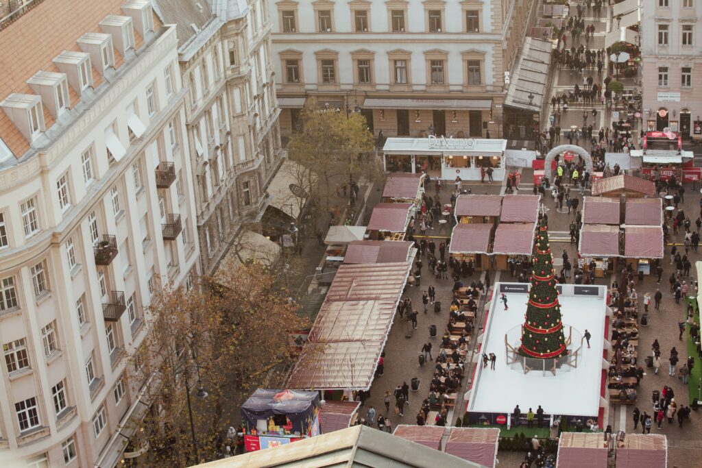 Aerial view of a Christmas market in Budapest with ice skaters skating around a Christmas tree.