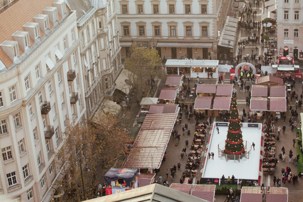 luftaufnahme eines weihnachtsmarktes in budapest mit schlittschuhläufern, die um einen weihnachtsbaum herumlaufen.