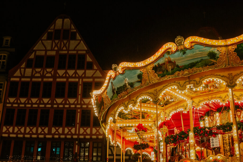 die lichter funkeln in warmen farben auf einem karussell vor einem traditionellen deutschen haus auf einem weihnachtsmarkt in frankfurt. 