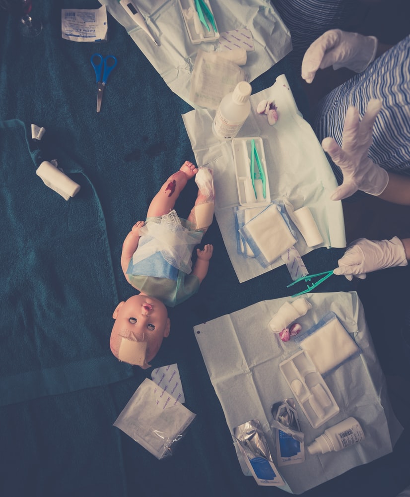 EHBO les tijdens de opleiding om gastouder te worden. Baby light op tafel met bloed. Oppas is bezig de baby te verzorgen met de daarvoor bestemde middellen zoals pleisters 