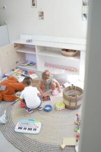 twee kindjes aan het spelen in een speelhoek met knuffels, boeken een speelgoed op de grond