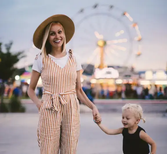 Au pair standing in front of fair with blond hair, hat and child