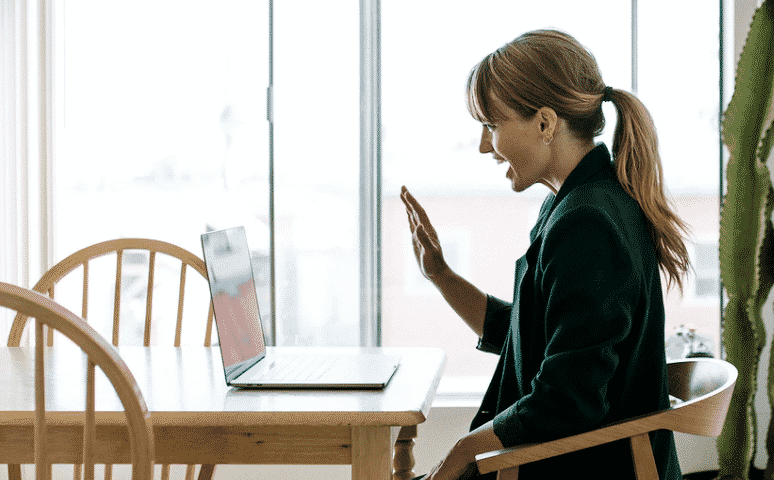 au pair nanny nina wordt geinterviewd door laptop die op de tafel staat. Ze zwaait naar het scherm