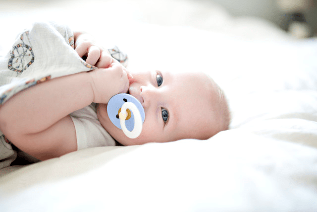 baby ligt op bed met een speen in zijn mond