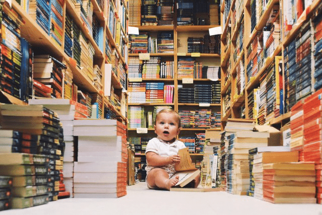 baby zit in een bibliotheek met een stapel boeken voor zich om ontwikkel sprongetjes te stimuleren 