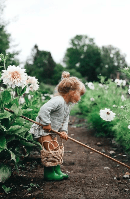 meisje van 4 met knotje werkt in de tuin met rieten mandje. witte Bloemen op de achtergrond.