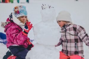 twee kinderen samen aan het buitenspelen in de winter om een sneeuwpop te maken 