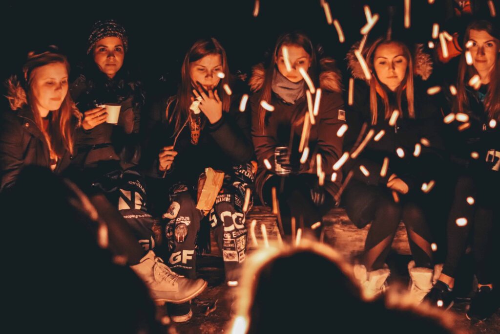 A group of friends is gathered around a bonfire outside in the winter to celebrate the holidays. 