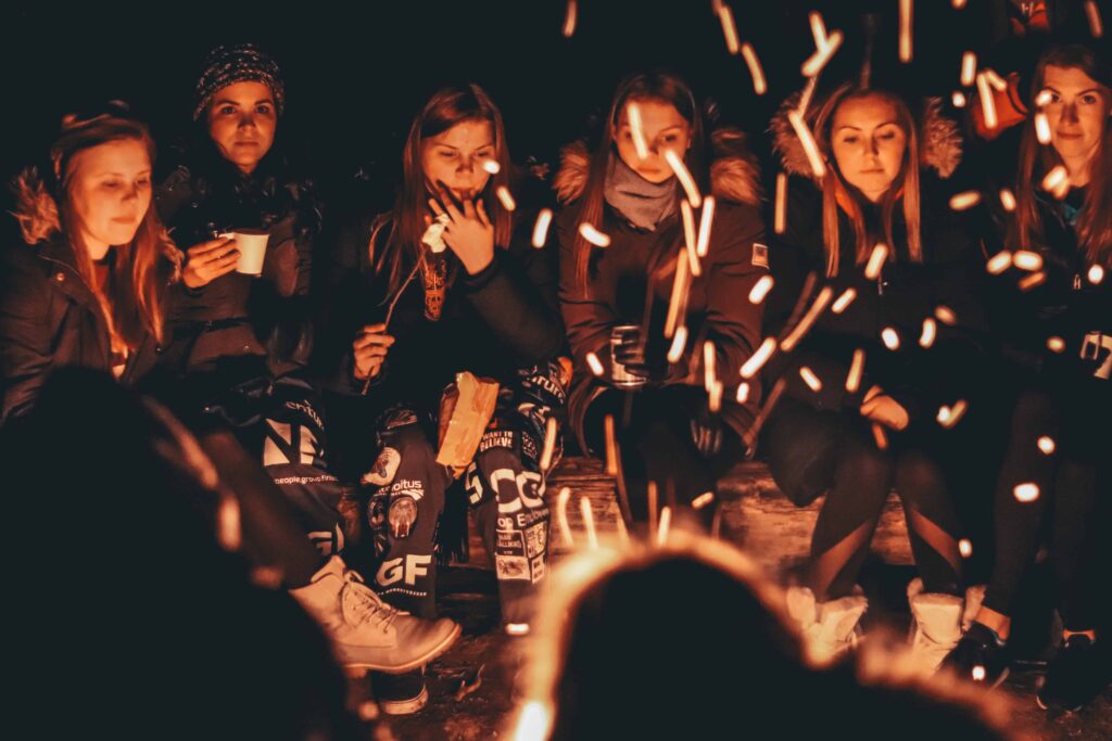 a group of friends is gathered around a bonfire outside in the winter to celebrate the holidays. 