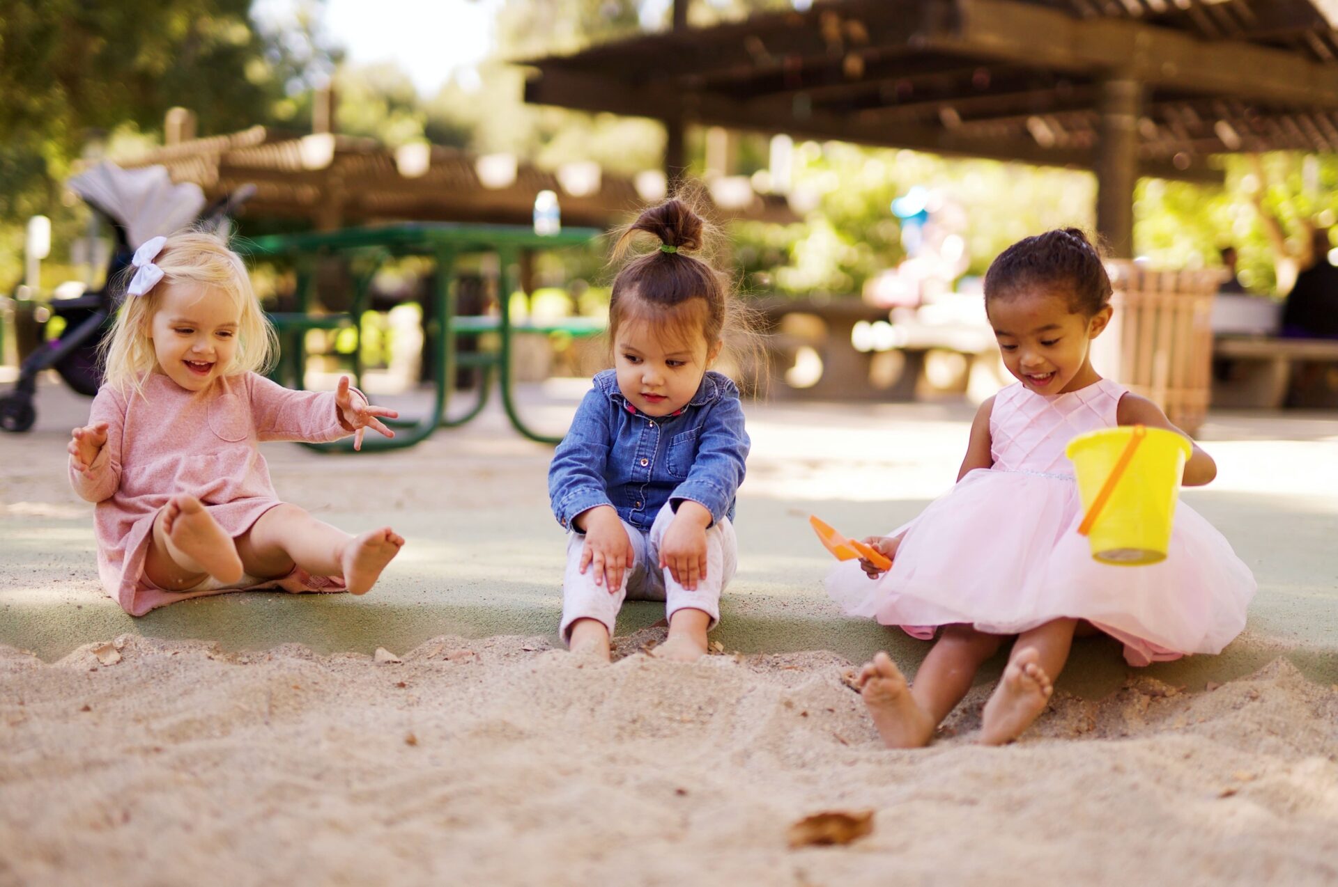 3 kindjes die in de zandbak zitten en aan het buitenspelen zijn in het zand met een emmer en een schep
