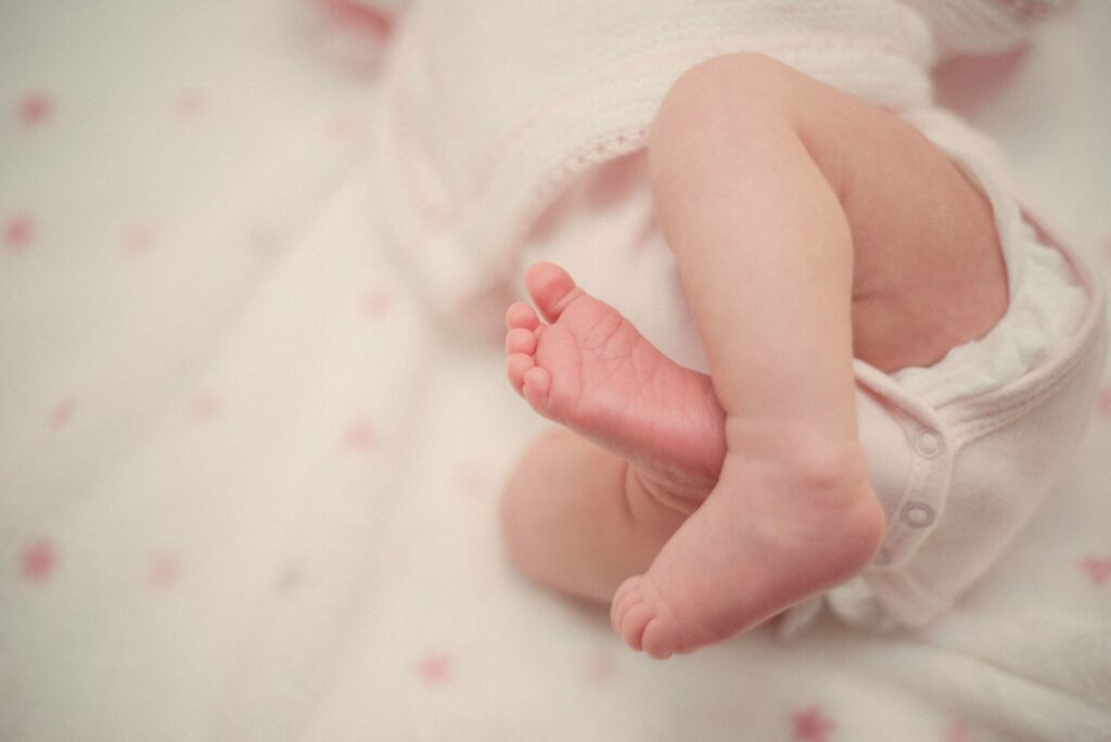 pasgeboren baby waar je alleen de voetjes van ziet terwijl ze op een kleedje ligt met een roze romper aan