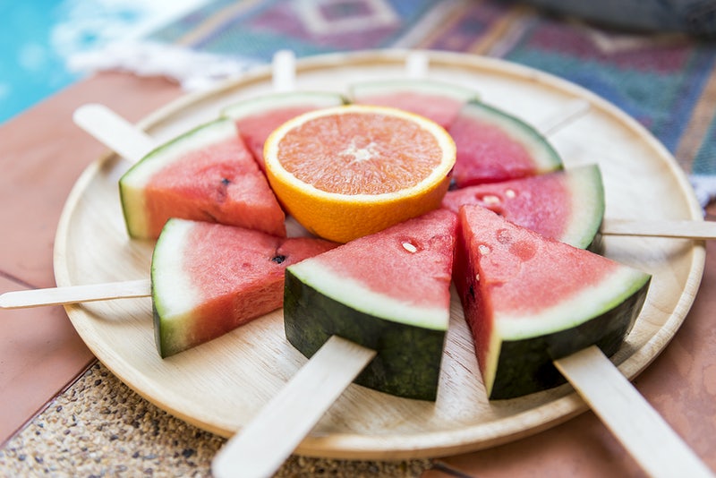 watermeloen en sinaasappel op een stokje op een houten bordje als snack voor tijdens de reis met kinderen 