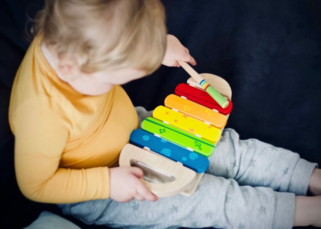 kindje in een grijze broek met geel shirt op de bank aan het spelen met een muziekinstrument