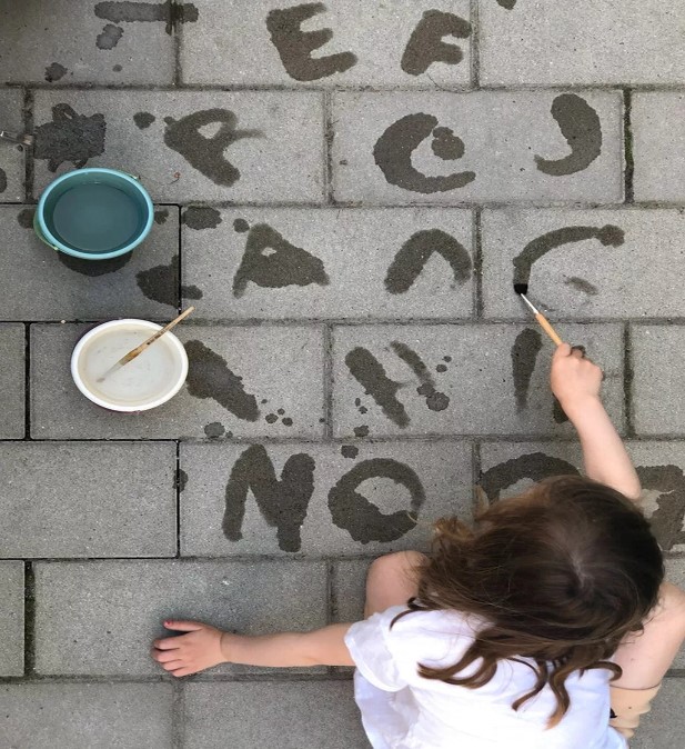 kind tekent letters op de stenen met een emmer water ernaast