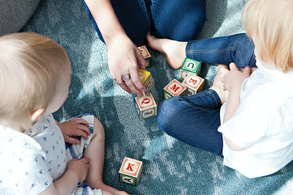 nanny die een oppasbaan heeft gevonden en nu met haar twee oppaskindjes op de grond met blokken aan het spelen is 