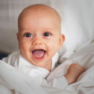 baby in een witte romper die op bed ligt en probeert te praten net als oudere kinderen